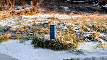 Thermos standing outside in the winter forest at dawn. Vacuum blue hiking flask. Travel concept, adventure, winter warming drink. photo
