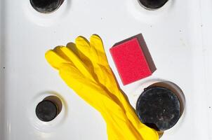 Dirty surface of gas stove, yellow gloves and washing sponge, top view. Household hygiene concept. photo