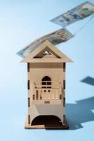 Model of wooden house and levitating hundred dollar bills. Concept for buying a home, mortgage, renting an apartment photo