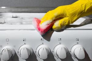 Woman cleans panel of the gas stove, close-up. Hygienic cleaning kitchen photo