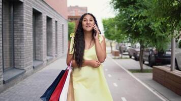 jong mooi meisje is wandelen in de omgeving van de stad na boodschappen doen en pratend Aan de telefoon. 4k video