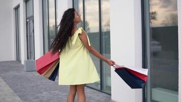 schön Mädchen Modell- im ein lange Gelb Kleid nach Einkaufen mit farbig Taschen im Hände haben ein gut Stimmung. schleppend Bewegung. hd video