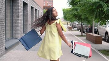 feliz jovem menina com grandes Sombrio cabelo dentro uma amarelo vestir regozija-se depois de compras com uma Boa humor. lento movimento. video