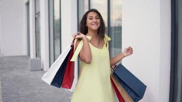 A beautiful girl in a yellow dress swirls with packages after shopping with a good mood. 4K. video