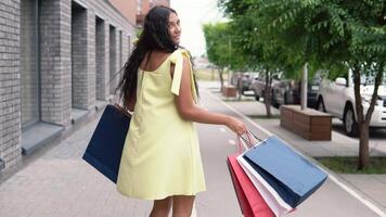 contento giovane ragazza con lungo buio capelli nel un' giallo vestito gioisce dopo shopping con un' bene umore. lento movimento. HD video