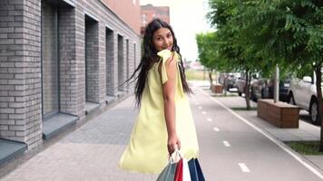 lindo jovem menina com grandes Sombrio cabelo dentro uma amarelo vestir depois de compras com uma Boa humor. lento movimento. hd video