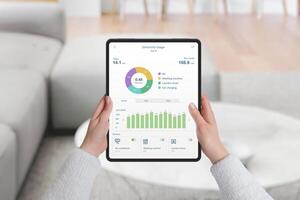 Hands holding tablet with home electricity monitoring app, analyzing consumption by device and month. Concept of energy efficiency and data tracking photo