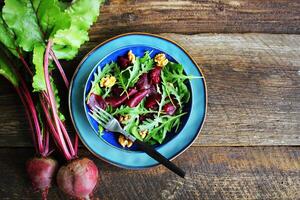 Healthy Beet Salad with fresh sweet baby spinach, arugula, nuts on wooden background . Top view photo