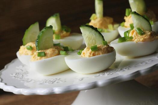 Spicy deviled eggs garnished with cucumber and leek on white plate. Wooden rustic background photo