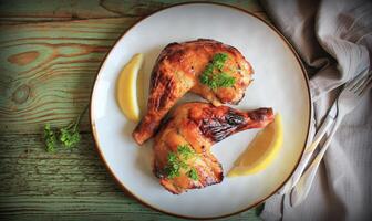 Grilled chicken leg quarters with lemon, parsley on white plate on wooden boards. Food background. Top view photo