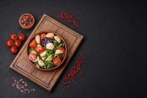 Delicious fresh caprese salad with mozzarella, tomatoes, greens with salt, spices and herbs photo