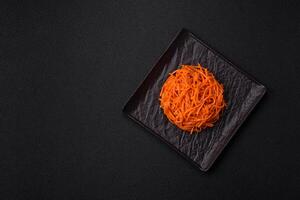 Tasty spicy Korean carrot with spices and herbs on a dark concrete background photo