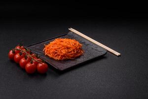 Tasty spicy Korean carrot with spices and herbs on a dark concrete background photo