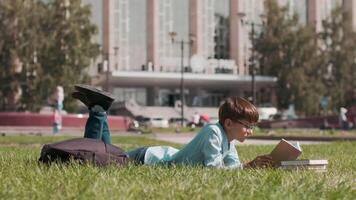 conectados Educação, costas para escola, feliz colegial, aprender aulas. estudante fazendo dever de casa usando livro didático deitado em a Relva perto escola video