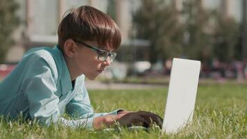 uppkopplad utbildning, tillbaka till skola, Lycklig skolpojke, lära sig lektioner. skol håller på med läxa använder sig av bärbar dator medan liggande på gräs nära skola video