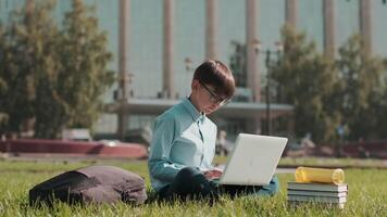 Online education, Back to school, Happy schoolboy, Learn lessons. Schoolboy doing homework using laptop while sitting on grass near school video