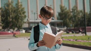 Online education, Back to school, Happy schoolboy, Learn lessons. A schoolboy with a backpack stands near the school and holds a textbook in his hands. Camera around video