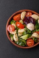 Delicious fresh caprese salad with mozzarella, tomatoes, greens with salt, spices and herbs photo