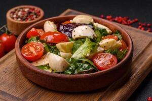 Delicious fresh caprese salad with mozzarella, tomatoes, greens with salt, spices and herbs photo