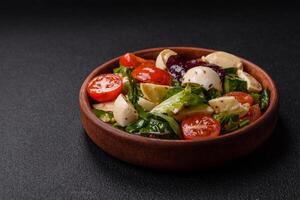 Delicious fresh caprese salad with mozzarella, tomatoes, greens with salt, spices and herbs photo