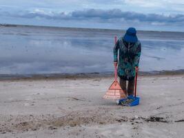 alguien quien es que lleva fuera basura limpieza ocupaciones alrededor el playa, verde tierra, costero limpiar día foto