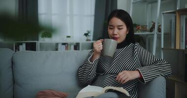 Footage dolly shot,Happy young asian woman drinking morning coffee or tea and reading in living room at home on weekend. Leisure and lifestyle,Free time video