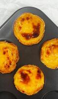 Lots of freshly baked Pastel de nata or Portuguese egg tart desserts in a baking dish. Pastel de Belme is a small pie with a crispy puff pastry crust and a custard filling. Small cupcake. photo