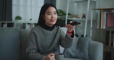 Footage steady shot,Happy woman holding remote control while enjoy sipping drinking coffee and watching movie on TV in living room,Leisure and lifestyle,Free time video