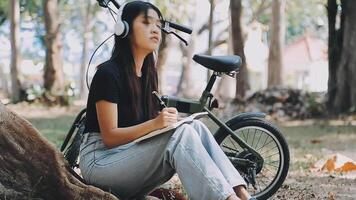 Lifestyle, education, adolescence. Teenage student in headphones with smartphone bicycle sitting in park, female looks at phone screen video