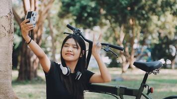 estilo de vida, educación, adolescencia. Adolescente estudiante en auriculares con teléfono inteligente bicicleta sentado en parque, hembra mira a teléfono pantalla video