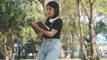 estilo de vida, educación, adolescencia. Adolescente estudiante en auriculares con teléfono inteligente bicicleta sentado en parque, hembra mira a teléfono pantalla video