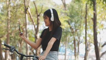 estilo de vida, Educação, adolescência. Adolescência aluna dentro fones de ouvido com Smartphone bicicleta sentado dentro parque, fêmea parece às telefone tela video