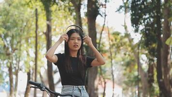 estilo de vida, educación, adolescencia. Adolescente estudiante en auriculares con teléfono inteligente bicicleta sentado en parque, hembra mira a teléfono pantalla video