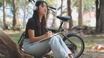 Lifestyle, education, adolescence. Teenage student in headphones with smartphone bicycle sitting in park, female looks at phone screen video