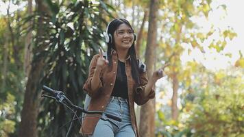 estilo de vida, educación, adolescencia. Adolescente estudiante en auriculares con teléfono inteligente bicicleta sentado en parque, hembra mira a teléfono pantalla video