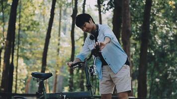 estilo de vida, educación, adolescencia. Adolescente estudiante en auriculares con teléfono inteligente bicicleta sentado en parque, hembra mira a teléfono pantalla video