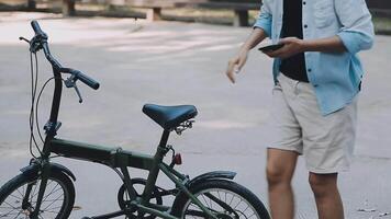 estilo de vida, educación, adolescencia. Adolescente estudiante en auriculares con teléfono inteligente bicicleta sentado en parque, hembra mira a teléfono pantalla video