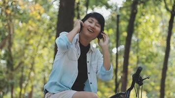 estilo de vida, educación, adolescencia. Adolescente estudiante en auriculares con teléfono inteligente bicicleta sentado en parque, hembra mira a teléfono pantalla video