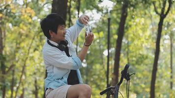 estilo de vida, Educação, adolescência. Adolescência aluna dentro fones de ouvido com Smartphone bicicleta sentado dentro parque, fêmea parece às telefone tela video