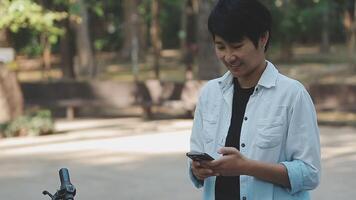 estilo de vida, educación, adolescencia. Adolescente estudiante en auriculares con teléfono inteligente bicicleta sentado en parque, hembra mira a teléfono pantalla video