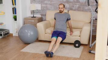 Forte cara fazendo tríceps Treinamento usando sofá dentro vivo quarto vestindo roupa de esporte. video