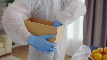 Close up of volunteer packing food in box for delivery wearing protective suit during gloabal covid-19 pandemic video