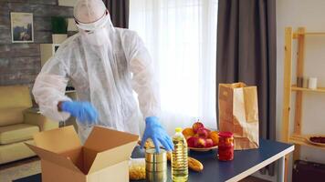 voluntario poniendo comida en caja vistiendo materiales peligrosos traje y guantes. video