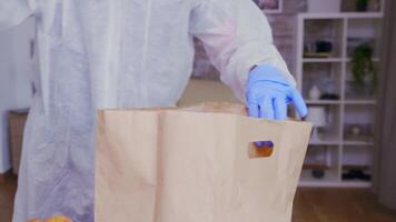 Close up of volunteer with gloves packing food wearing protective suit against coronavirus. video