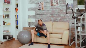 Athletic man doing biceps curl sitting on sofa at home. video