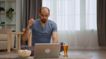 Zoom in shot of angry man on a video call during coronavirus lockdown drinking beer.