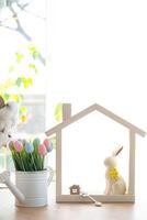 Key and tiny house of cozy home with Easter decor with rabbit and eggs on table of kitchen. Building, design, project, moving to new house, mortgage, insurance, rent and purchase real estate photo