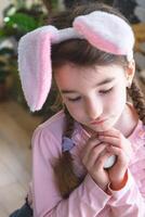 un linda niña con rosado conejito orejas linda Pascua de Resurrección retrato de un niño en el interior foto