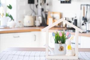 Key and tiny house of cozy home with Easter decor with rabbit and eggs on table of kitchen. Building, design, project, moving to new house, mortgage, insurance, rent and purchase real estate photo