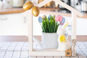 Key and tiny house of cozy home with Easter decor with rabbit and eggs on table of kitchen. Building, design, project, moving to new house, mortgage, insurance, rent and purchase real estate photo